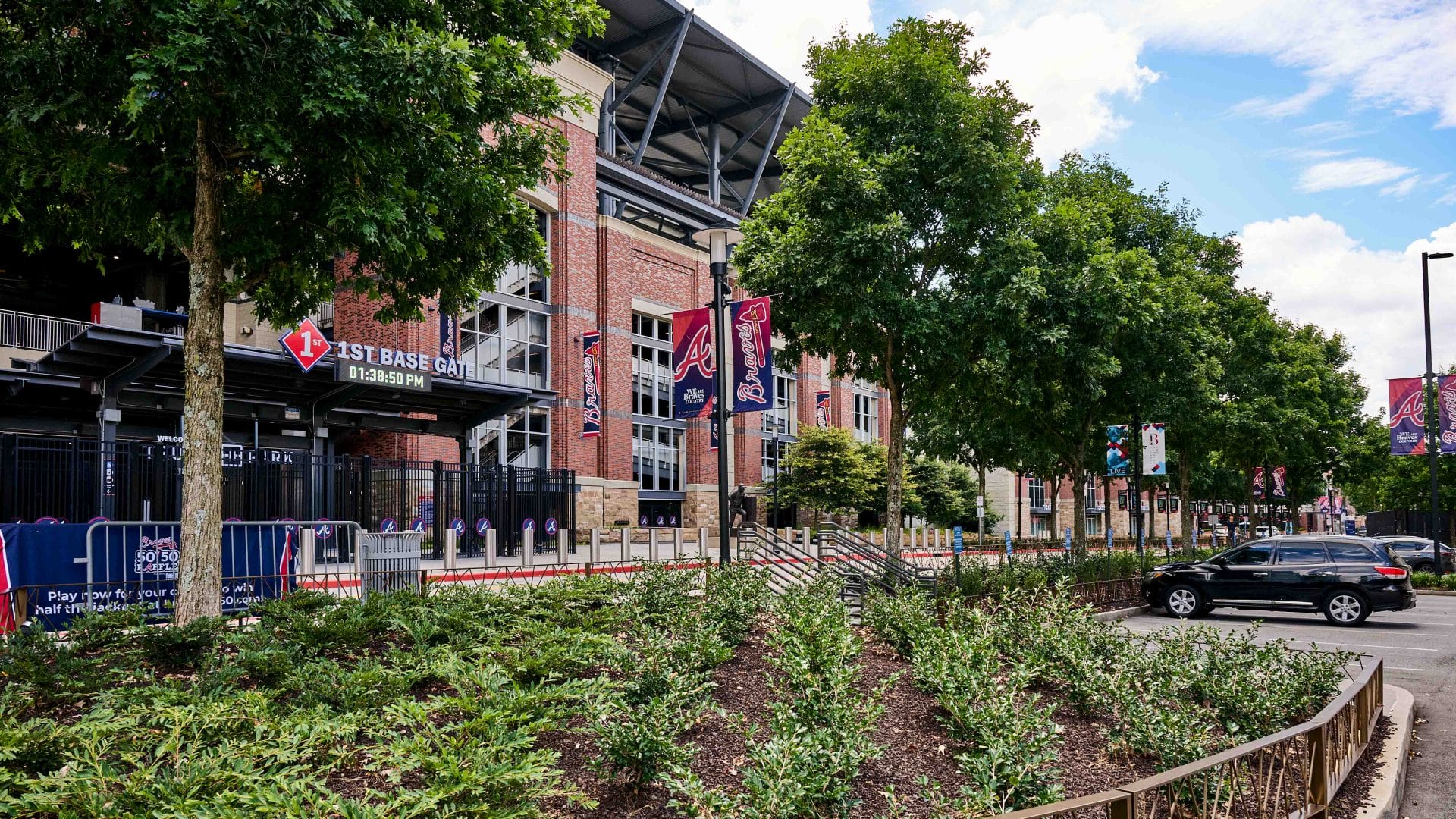 Commercial landscape installation with trees, shrubs, and mulch beds outside a large stadium entrance.