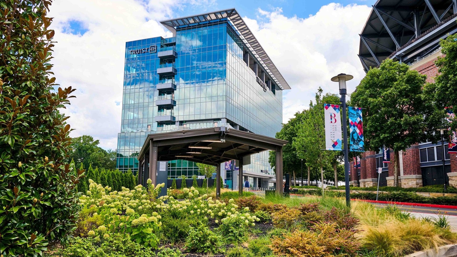Commercial landscape design with ornamental grasses, shrubs, and planting beds outside a modern office building near a stadium district.