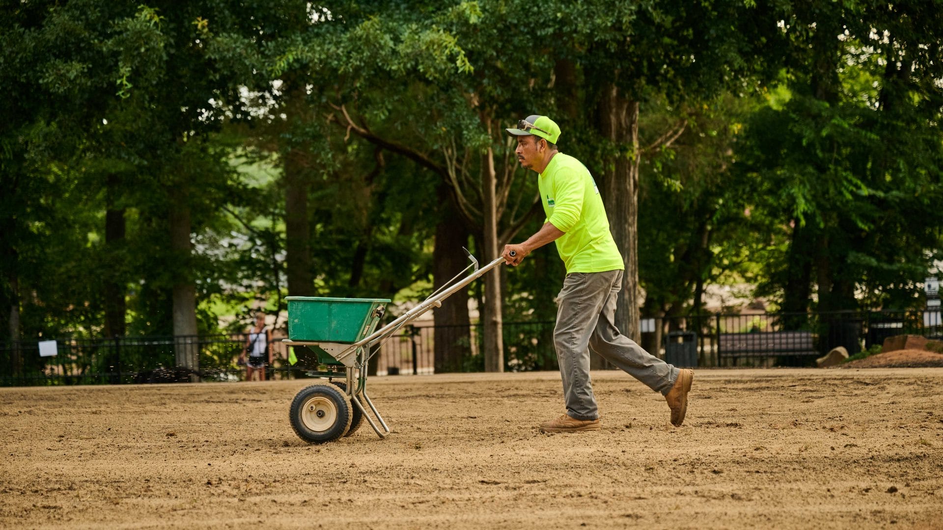 Landscaping professional spreading grass seed with a broadcast spreader during lawn installation.